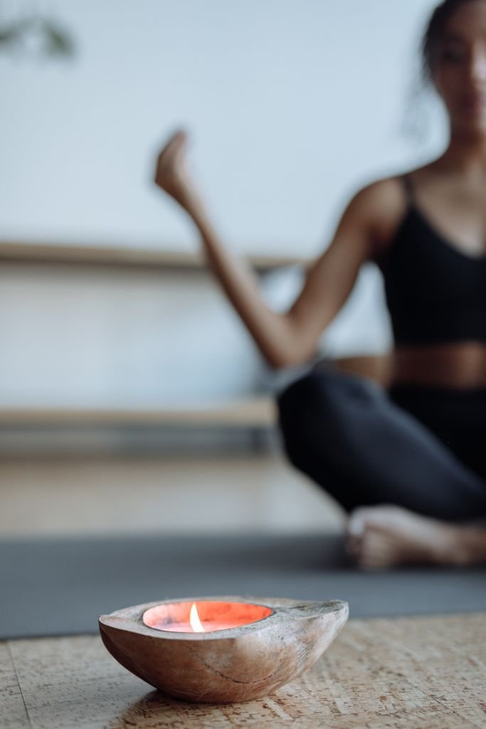 A woman meditates on a yoga mat with a lit candle in focus, creating a calming atmosphere.